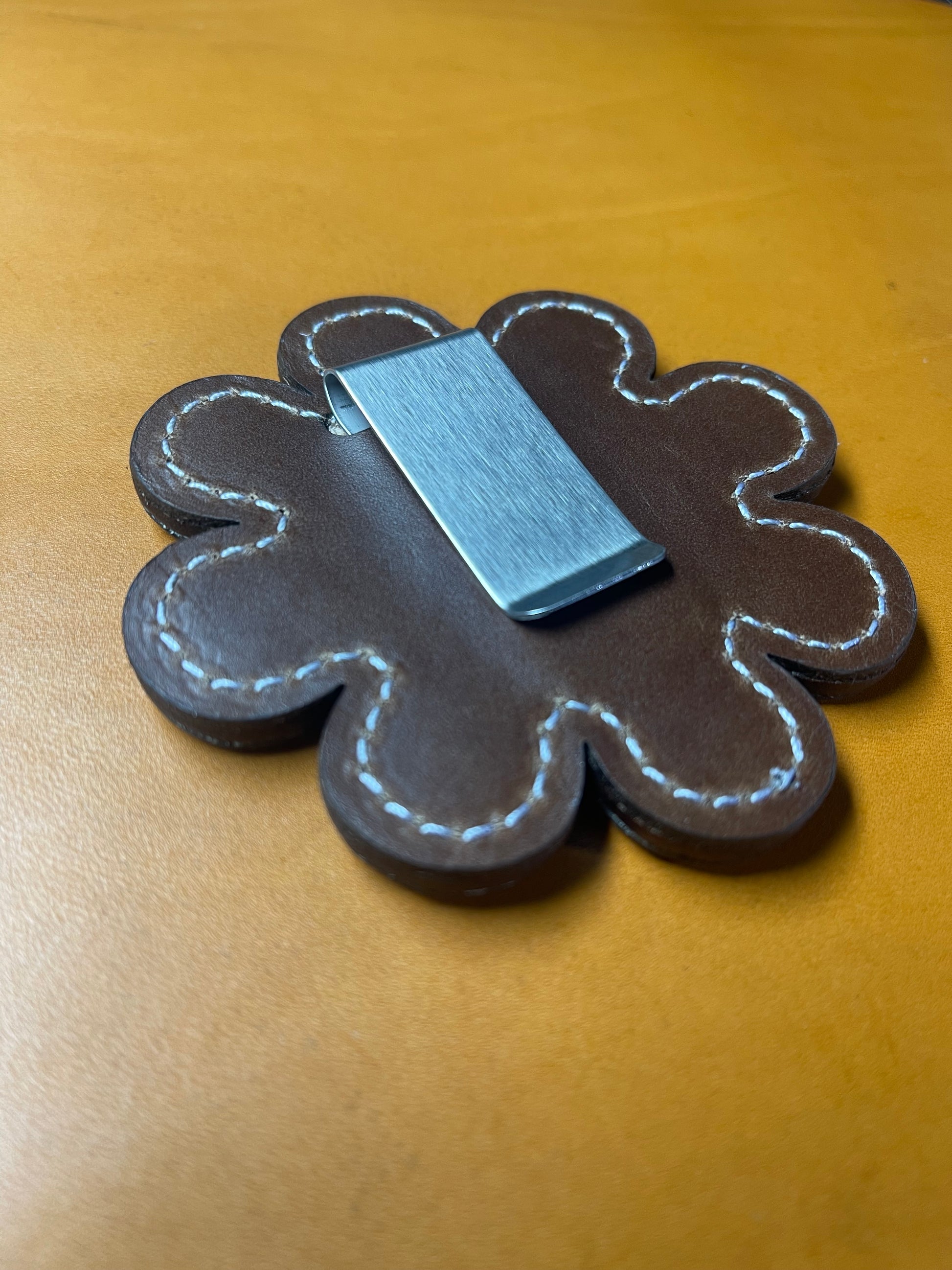 Close-up of the brown leather on back of daisy-shaped design with precise stitching and a stainless steel clip