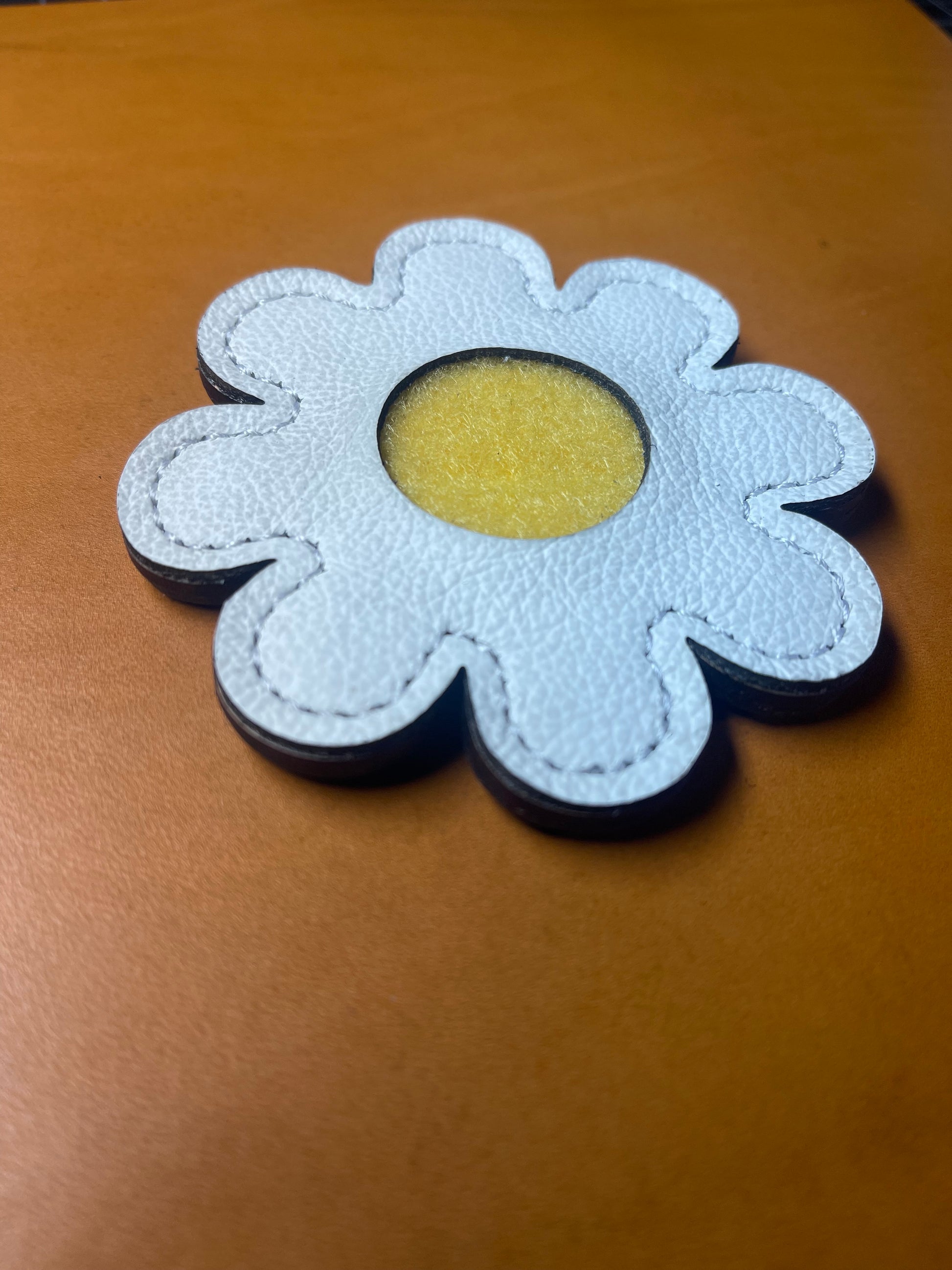 Close-up of the pebbled white leather texture and daisy-shaped design with precise stitching.