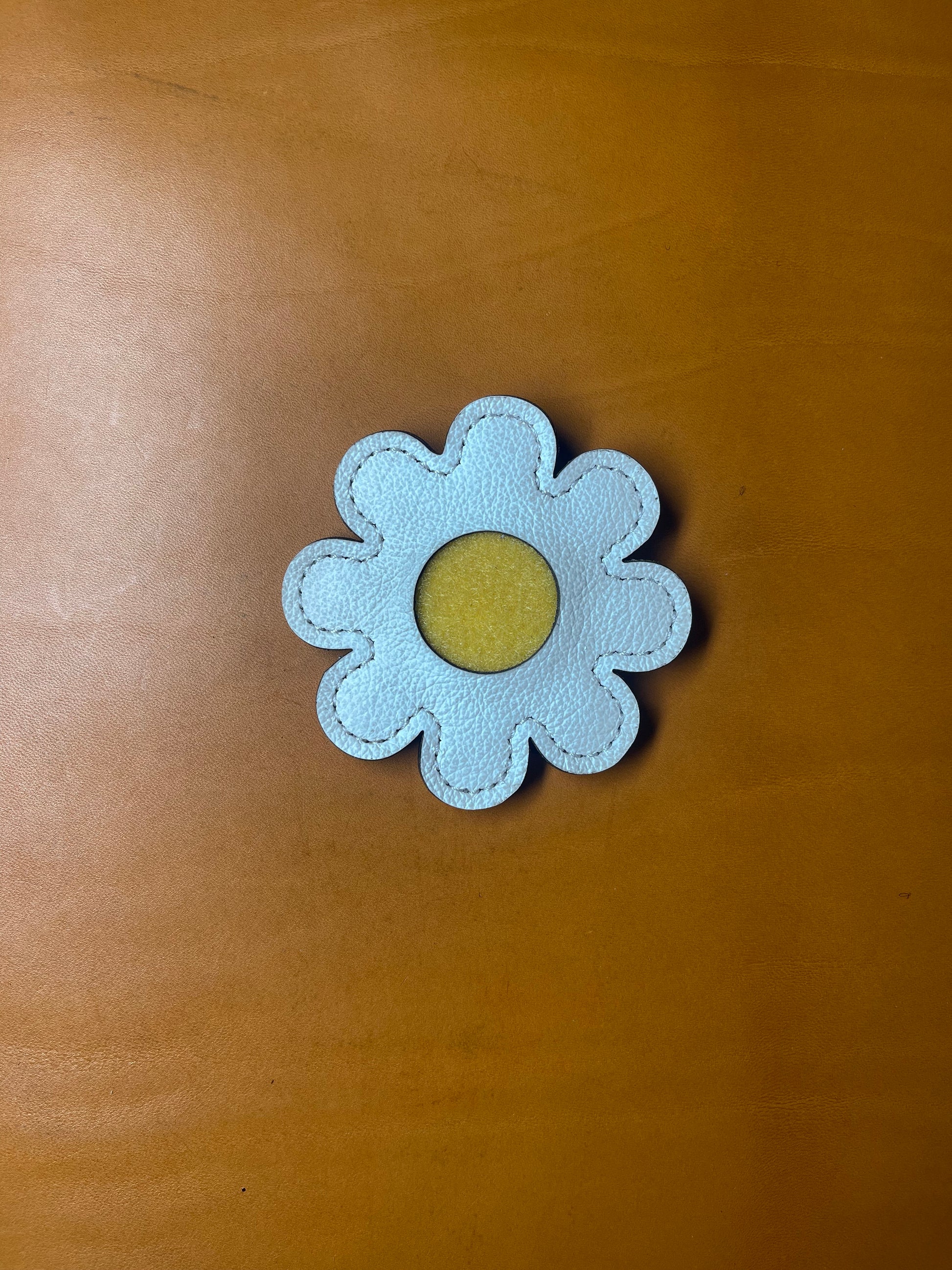 White pebbled leather glove holder shaped like a daisy, featuring a stainless steel clip for attaching to golf bags, belts, pockets and waistbands.